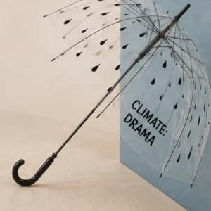 Paraguas transparente abierto con diseño de gotas negras y la frase "CLIMATE DRAMA" impresa en el panel frontal.