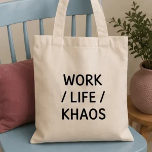 Bolsa de tela color crema sobre una silla azul, con el texto "WORK / LIFE / KHAOS" impreso en letras negras.
